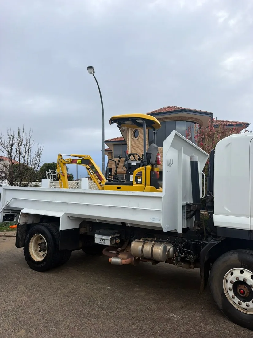 Mini excavator loaded on the back of a tipper truck on a suburban street