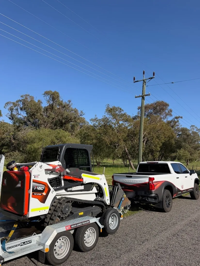 Bobcat T450 loaded on a plant trailer behind a ute, parked on a rural road
