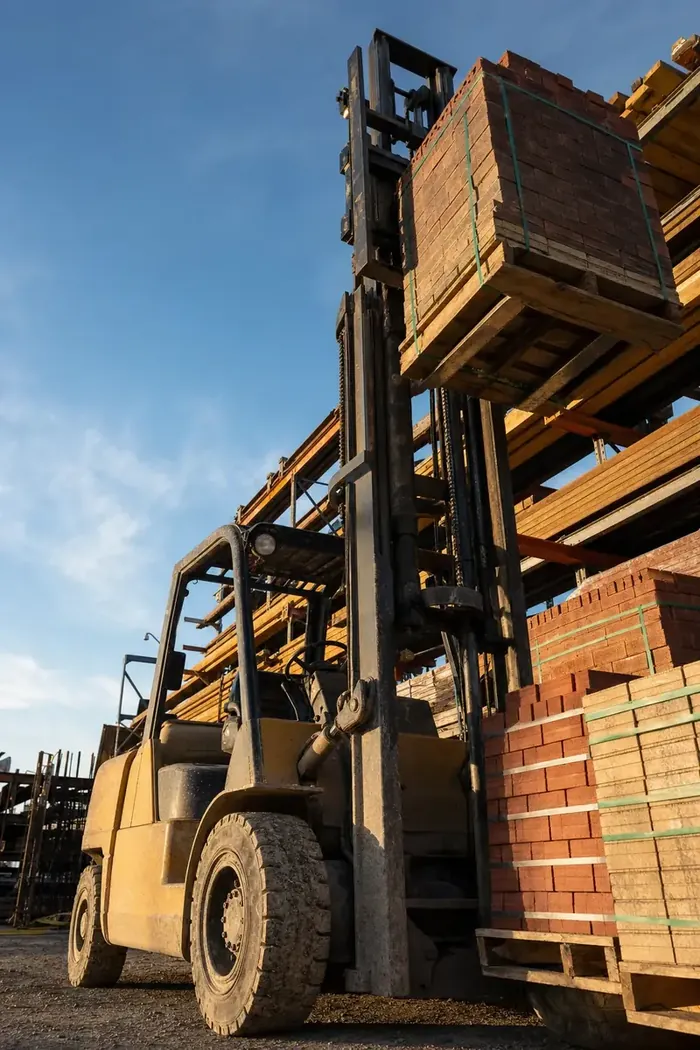 Forklift with its mast raised placing a pallet of bricks on a stack in a Perth builders yard