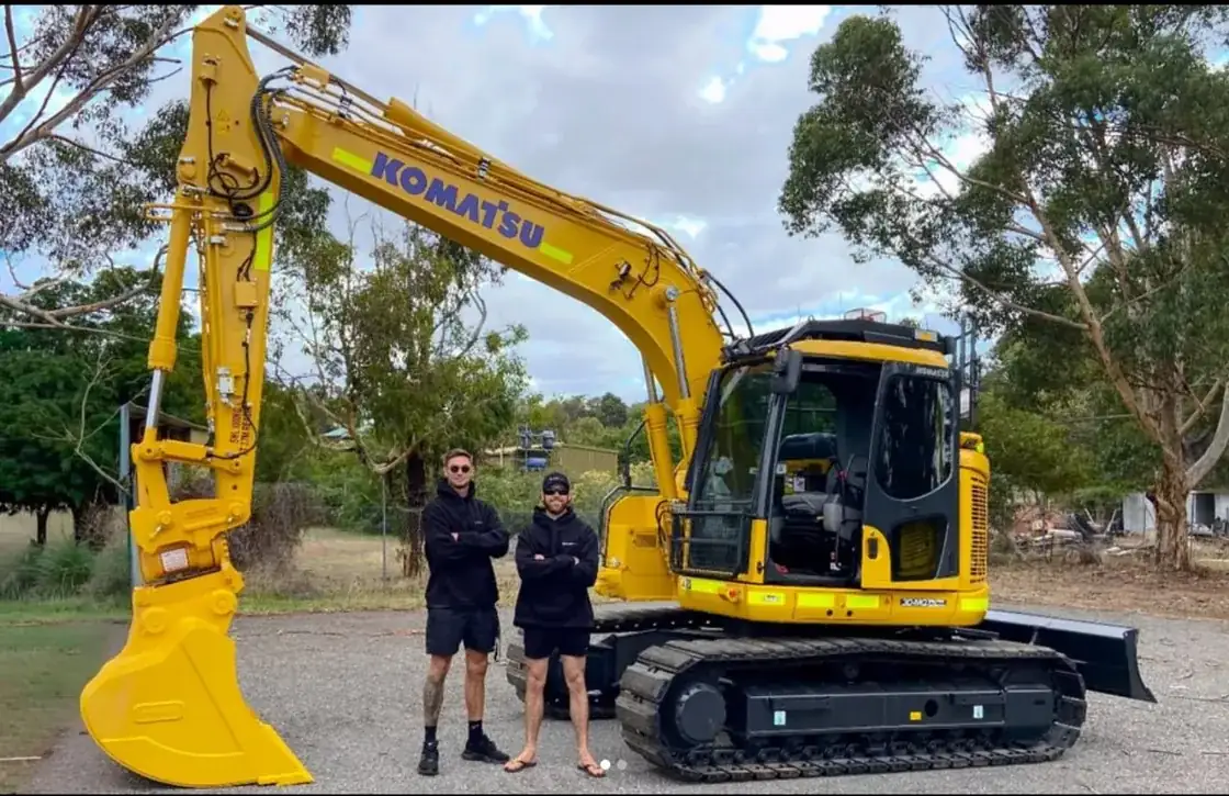 Billy and Daniel, owners of Plant Hire Perth, standing with their excavator on a Perth site