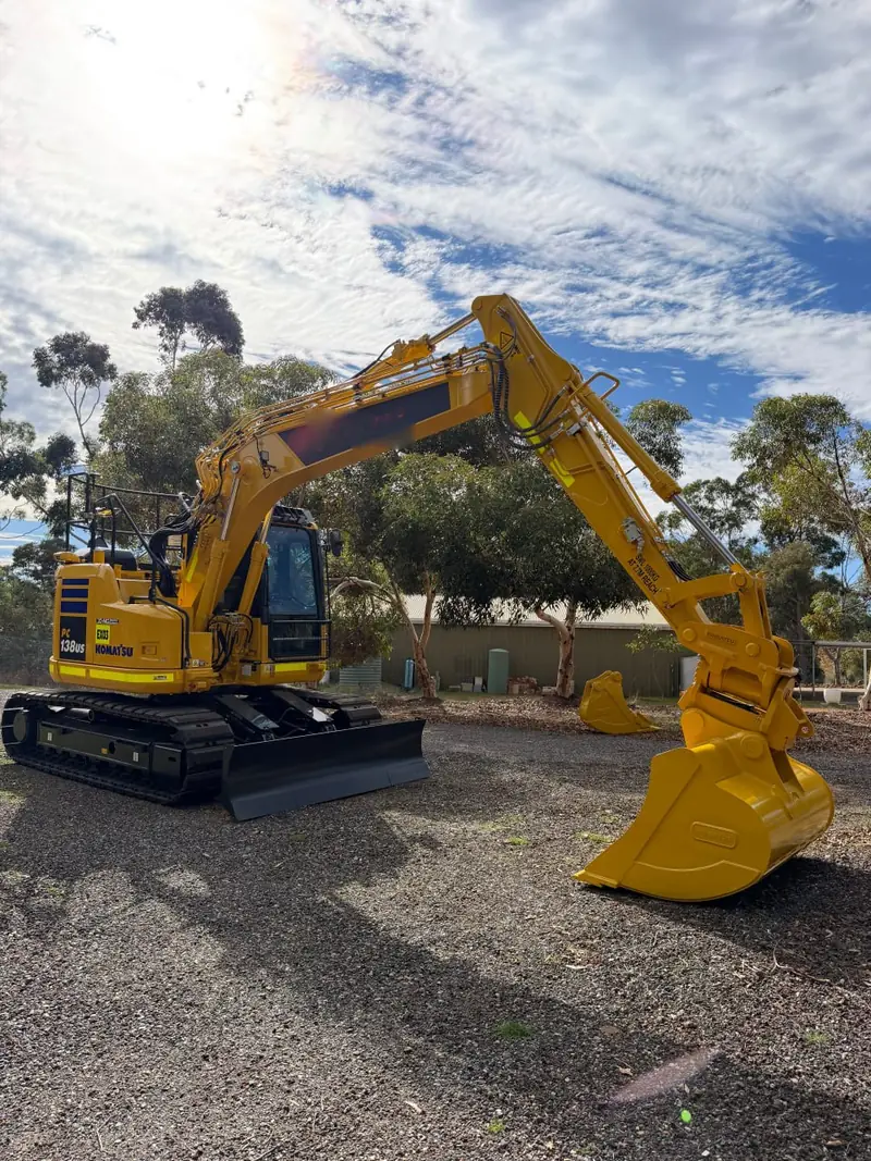 Komatsu 13.8 tonne excavator parked with a batter bucket and a digging bucket sitting beside it
