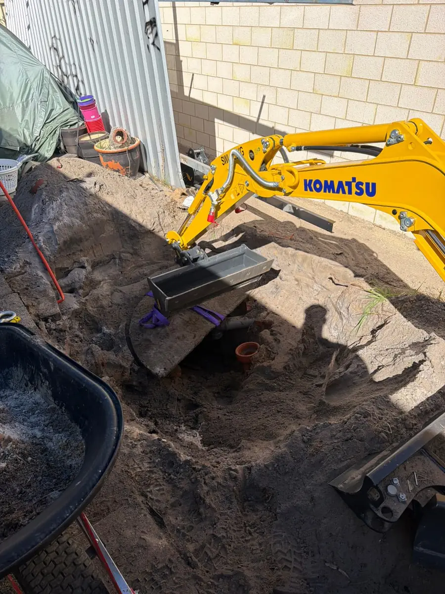 Excavator bucket working the floor of a trench directly over an exposed pipe run