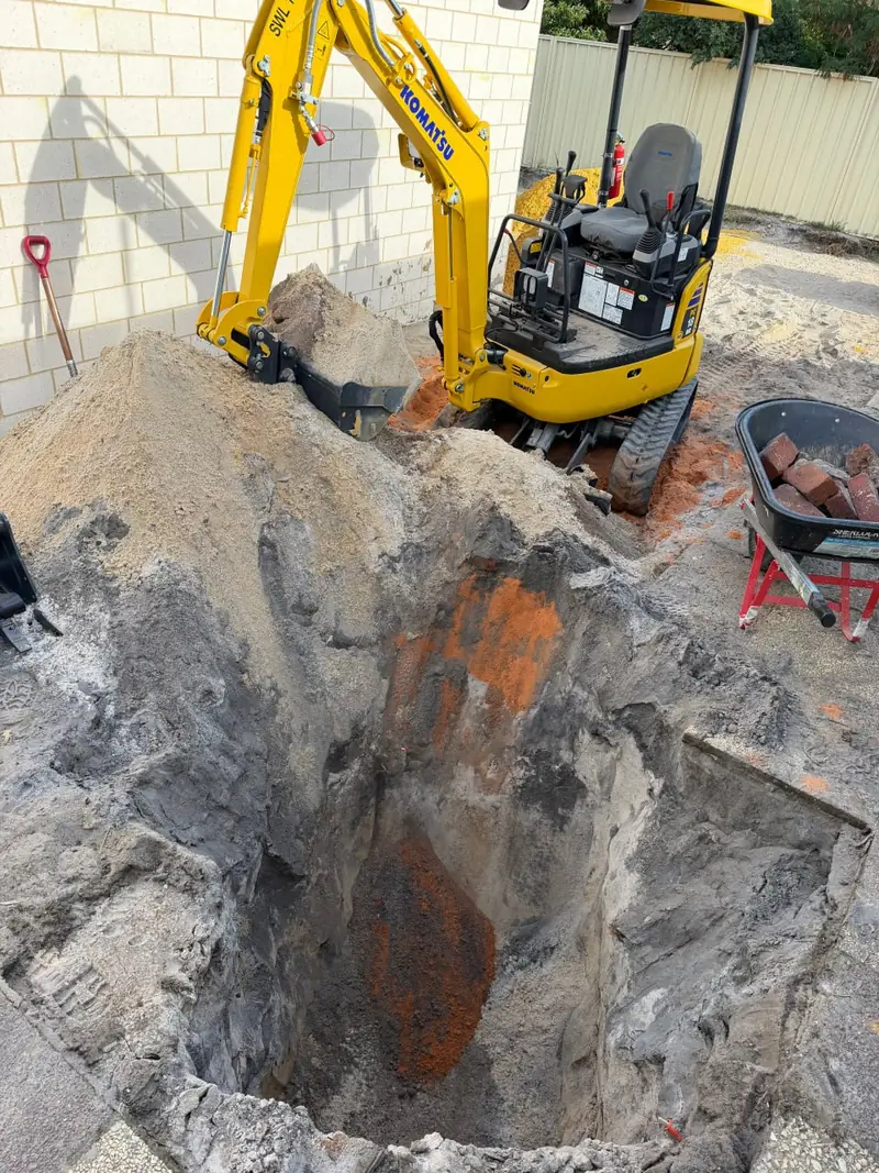 Open trench showing sand, limestone and a rust coloured seam through the excavated face
