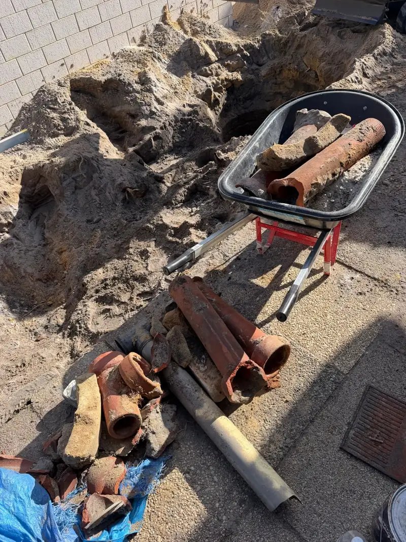 Broken lengths of old earthenware pipe stacked beside a wheelbarrow after being dug out