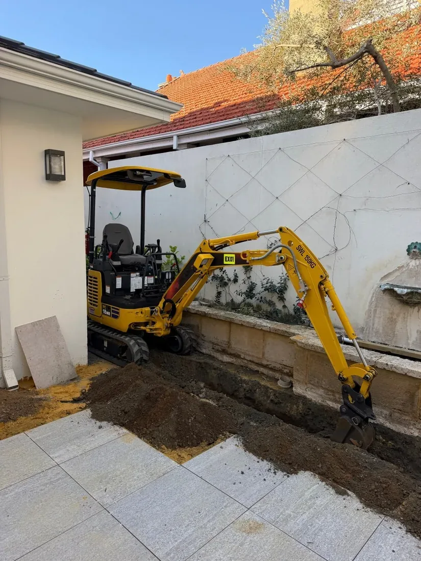 1.8 tonne excavator digging a trench in the narrow gap between a house wall and a boundary wall